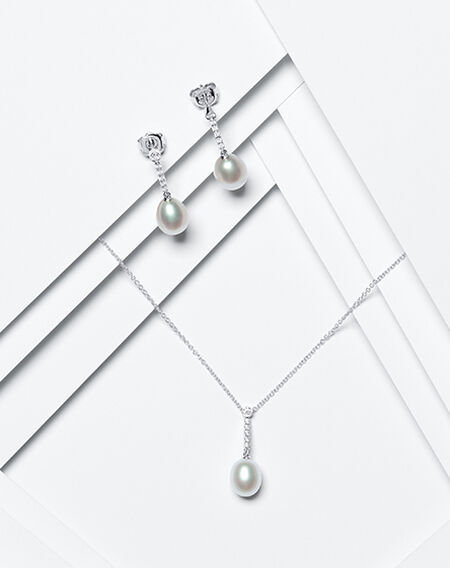 A pair of diamond and pearl drop earrings and pendant from Birks on a white layered background.